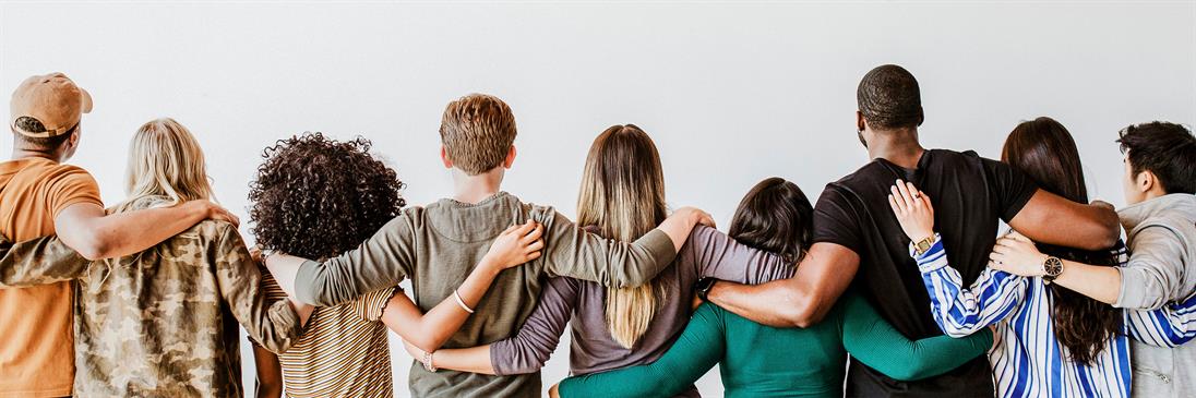 Eine Gruppe von Menschen unterschiedlichen Geschlechts und Herkunft die von hinten gezeigt werden und die Arme umeinander gelegt haben.